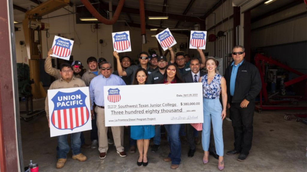 A group of SWTJC students huddle around the $380,000 contribution check from UP. Behind the check are, from left, Ken Kuwamura (in light blue), Manager-Talent Acquisition, UP; Raquel Espinoza, Senior Director-Public Affairs, UP; Esmerelda Arreola, SWTJC Diesel Technology Program Lab Assistant; Texas State Rep. Eddie Morales and his wife, Helen Morales; and Tom Blevins, Superintendent-Train Operations, UP. (Caption and Photograph Courtesy of UP)
